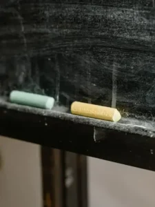 Detailed shot of colored chalk pieces on a dusty blackboard ledge.